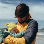 man in black jacket carrying baby in yellow hoodie