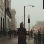 person wear black coat and backpack walking on sidewalk