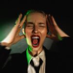 A woman in a suit and tie with her hands on her head