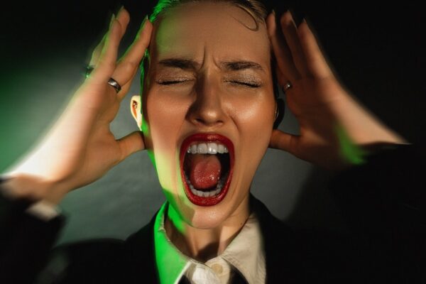 A woman in a suit and tie with her hands on her head